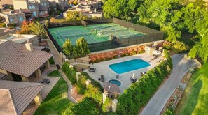 Vista aerea di una proprietà residenziale con campo da tennis, piscina e giardino curato.