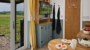 A room with a television, wooden cabinet, and a table with plates and a teapot. - Daisy Shepherd's Hut, North Molton (North Molton)