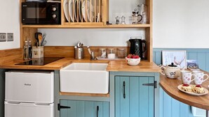 A kitchen with wooden shelves, a microwave, a sink, and a refrigerator. - Daisy Shepherd's Hut, North Molton (North Molton)