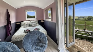 Une chambre à coucher avec un lit, deux fenêtres, une chaise et un balcon donnant sur la campagne.