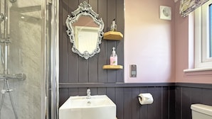 Une salle de bain équipée d’une douche, d’un lavabo, de toilettes, d’un miroir et d’une étagère où sont rangés les articles de toilette.