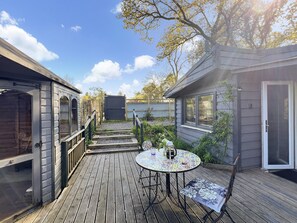 Une terrasse en bois avec une table ronde et des chaises, entourée d’une clôture en bois et d’un petit jardin.