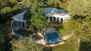 Luchtbeeld van een modern huis met een zwembad, zonnepanelen en een patio omringd door weelderige begroeiing.