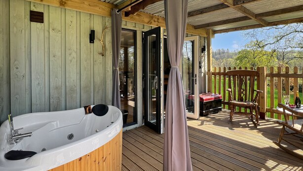 Eine Holzterrasse mit Whirlpool, einem Holzstuhl und einem Tisch mit Flasche und Glas.