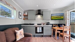 A compact living space with a kitchenette, a dining area, and a sofa with a cushion. - Robins Nest Lodge, South Molton (South Molton)