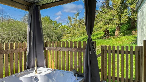 A hot tub on a wooden deck with a wooden fence and greenery in the background. - Robins Nest Lodge, South Molton (South Molton)