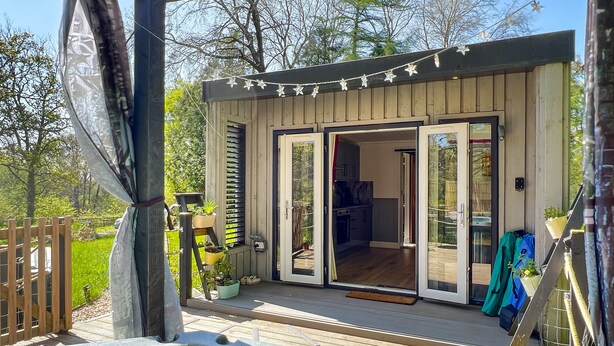 Une terrasse en bois avec un jacuzzi, une cuisine extérieure couverte et une porte-fenêtre coulissante donnant sur un espace de vie.