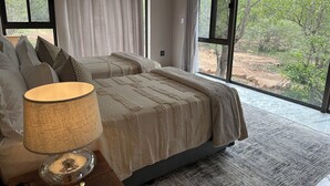 Una camera da letto con un letto grande, una lampada da comodino e vista su un paesaggio naturale attraverso ampie finestre.