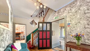A spacious living area with a wooden floor, a teal sofa, and a staircase leading to an upper level.