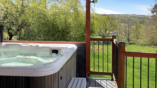 A hot tub on a wooden deck with a view of a green landscape.