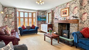 A cozy living room with a fireplace, floral wallpaper, and comfortable seating.