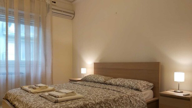 A bedroom with a bed, two bedside lamps, a nightstand, and a window with curtains. - COCO Apartments (Catania)