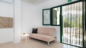A room with a beige sofa, a small white table with a cup, a green-framed window, and a wall-mounted air conditioner. - Cozy home in Rogoznica with WiFi (Rogoznica)