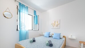 A bedroom with a bed, a window with curtains, a bedside table, a wall-mounted mirror, and a framed artwork. - Cozy home in Rogoznica with WiFi (Rogoznica)