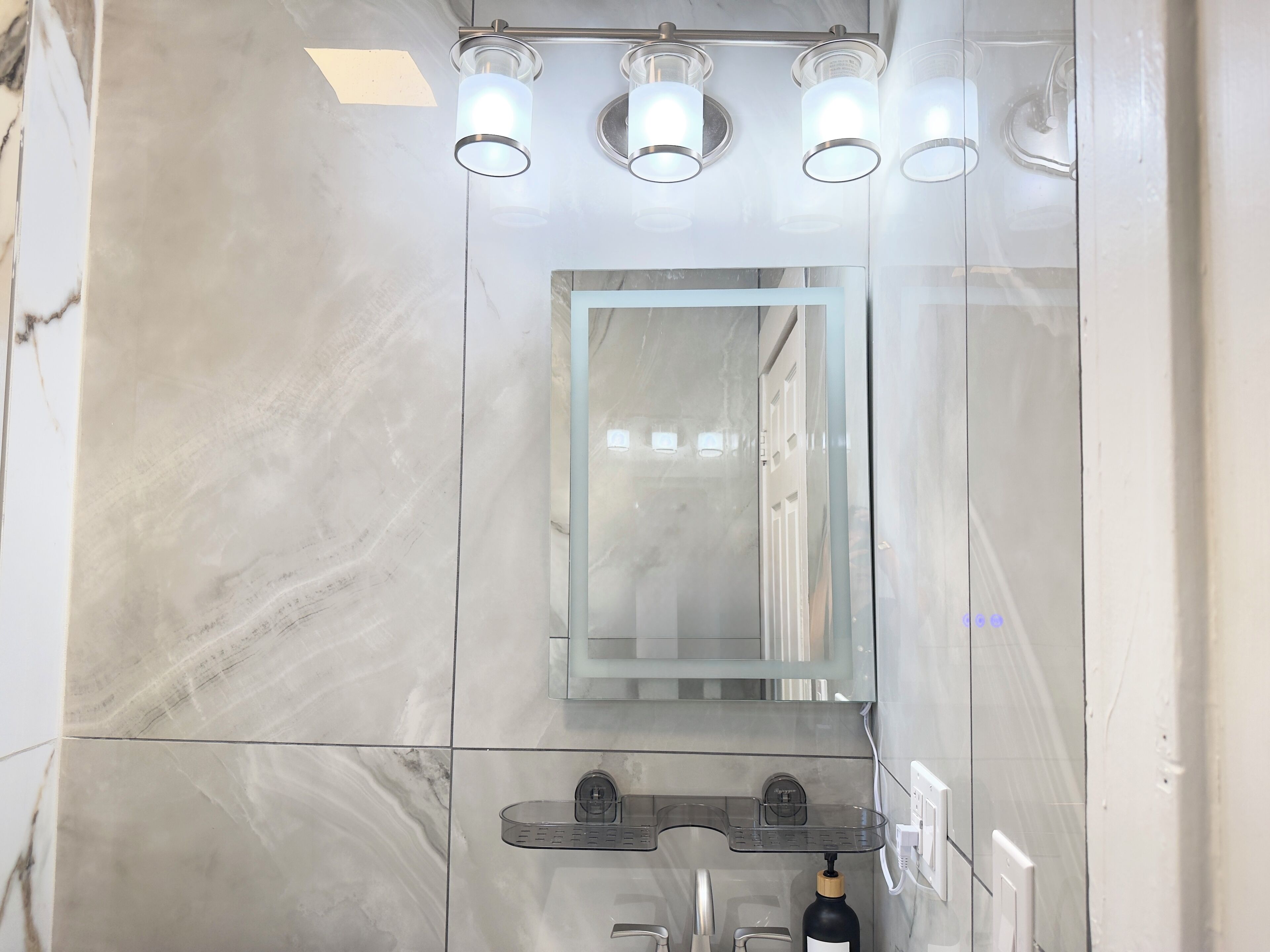 Une salle de bain moderne avec un grand miroir, une douche en verre et un lavabo doté d’un distributeur de savon.