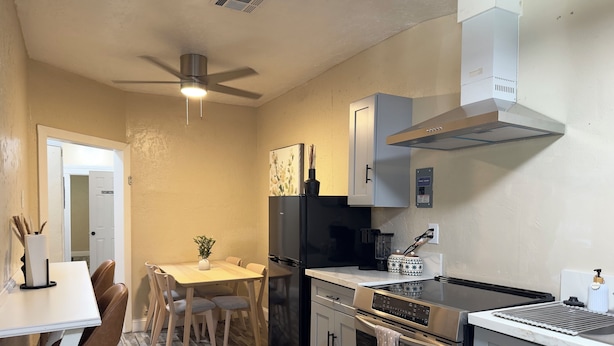 A compact kitchen with a dining area, a ceiling fan, a black refrigerator, a stove, and a microwave. - Sequoia Escape 3BR Home w/ King Bed & In-Unit Laundry (Visalia)