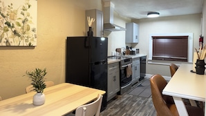 A compact kitchen with a black refrigerator, a microwave, and a stove. There is a dining table with chairs and a small potted plant. - Sequoia Escape 3BR Home w/ King Bed & In-Unit Laundry (Visalia)