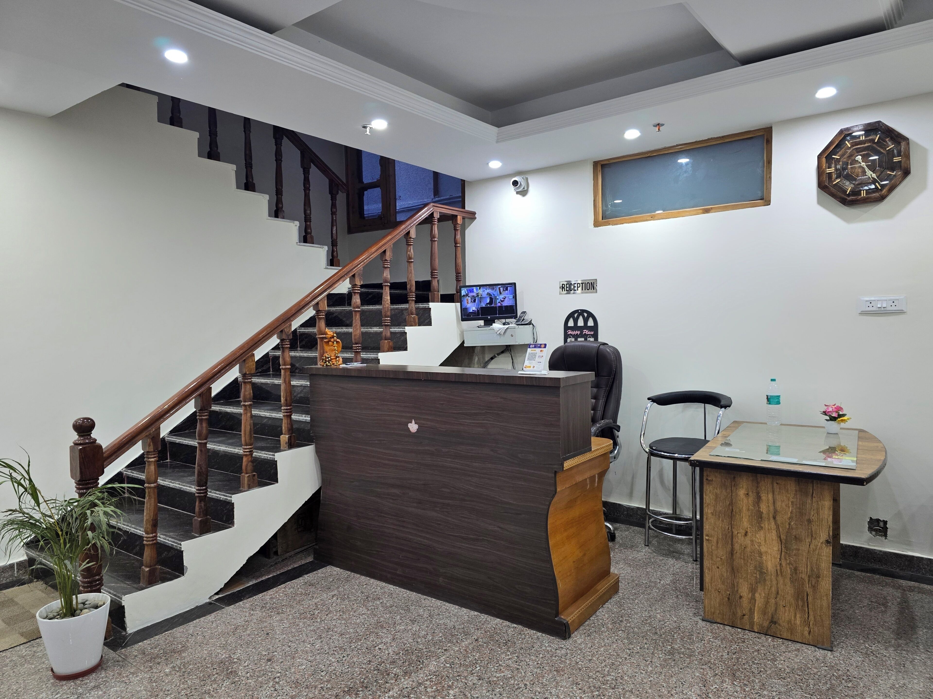 A reception area with a wooden reception desk, a computer, a clock, and a staircase.