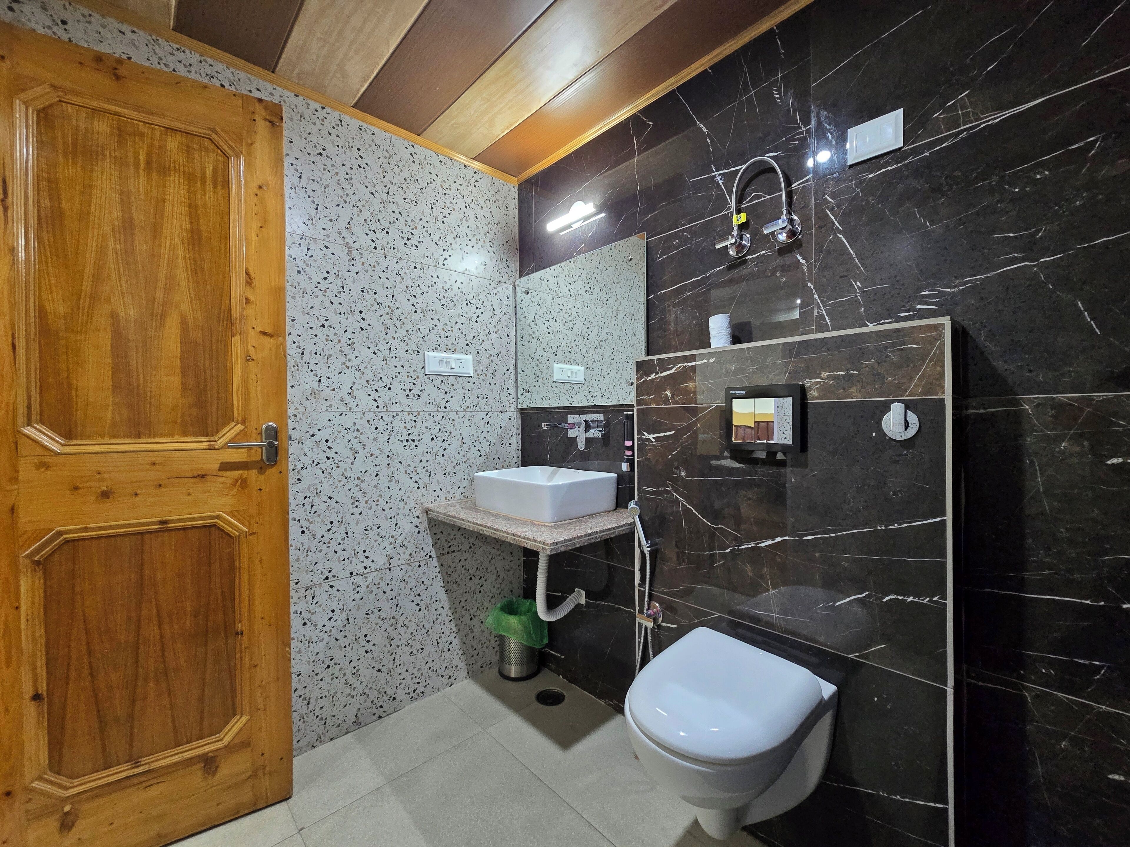 Un bagno con porta in legno, un lavandino, un water e una doccia con pannello di controllo.