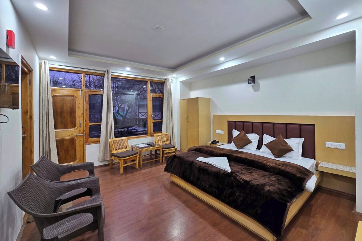 Habitación de hotel con una cama grande, un escritorio y una silla. Tiene una ventana con cortinas, y el suelo es de madera.