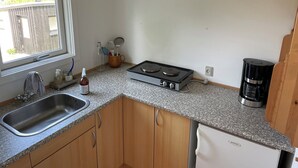 A compact kitchen with a sink, stove, coffee maker, and wooden cabinets.