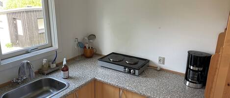 A compact kitchen with a sink, stove, coffee maker, and wooden cabinets.