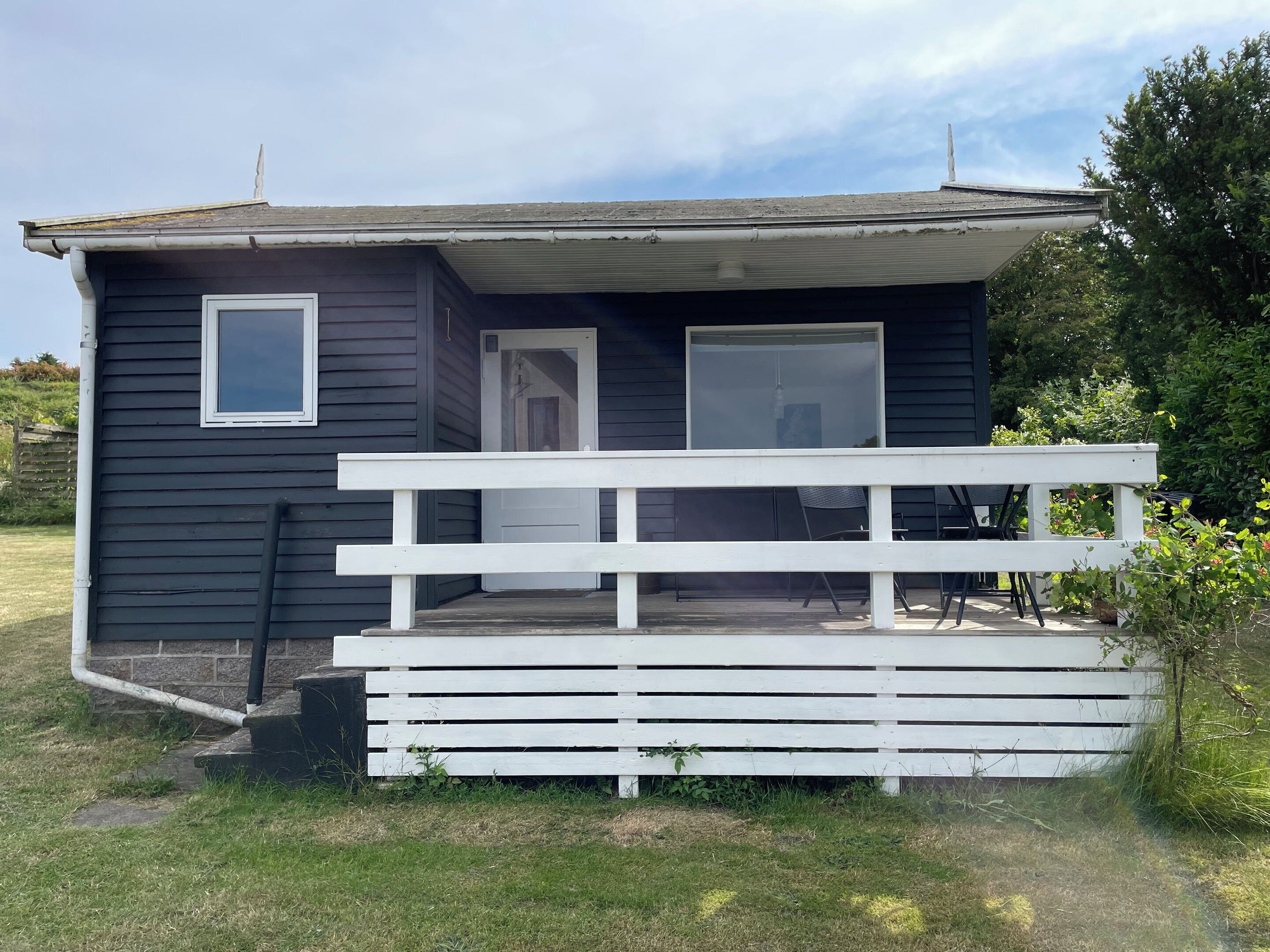 A small, dark-colored cabin with a white porch and a door.