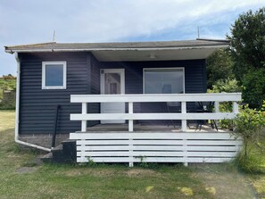 A small, dark-colored cabin with a white porch and a door.