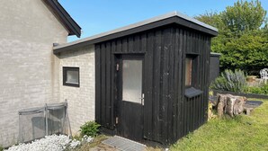 A small black wooden structure with a door and window, adjacent to a building with a stone facade.