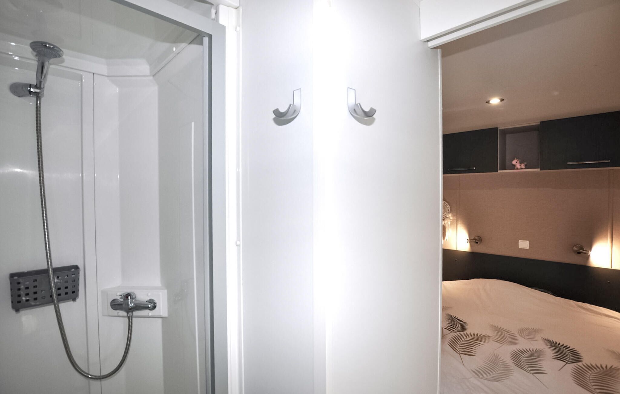 A bathroom with a glass shower enclosure, a towel rack, and a bed with a patterned bedspread.