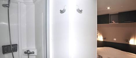 A bathroom with a glass shower enclosure, a towel rack, and a bed with a patterned bedspread.