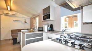 A modern kitchen with a gas stove, microwave, and toaster. There is a sink and a window providing natural light. - Mobile Home proche mer piscine (Narbonne Plage)