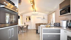 A compact kitchen with modern appliances, a dining area with a table and chairs, and a cozy living space with a sofa. - Mobile Home proche mer piscine (Narbonne Plage)