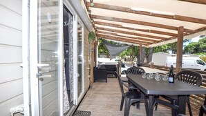 An outdoor patio with a table and chairs, a grill, and a covered area with a canopy. - Mobile Home proche mer piscine (Narbonne Plage)