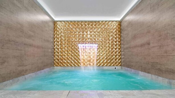 A small, rectangular indoor pool with a geometric patterned wall and a ceiling light.