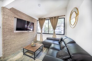 Un salon moderne avec un mur en pierre, un téléviseur à écran plat, un canapé en cuir, une table basse et une fenêtre avec des rideaux.