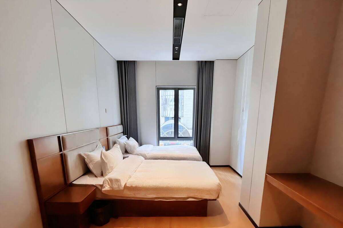 A modern bedroom with a large bed, a nightstand, and a window with curtains.