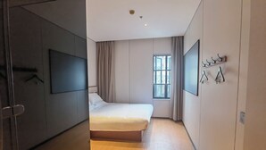 Een moderne slaapkamer met een groot bed, een aan de muur bevestigde televisie, een raam met gordijnen en een kapstok.