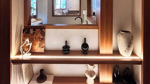 Een houten plank met decoratieve voorwerpen, een spiegel die een keuken weerspiegelt, en een vaas.