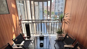 Een moderne wachtruimte met zwarte stoelen en een tafel, grote ramen bieden uitzicht op hoge gebouwen en een heldere lucht.