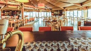 A spacious restaurant with multiple tables and chairs, a large windowed wall, and a prominent brass espresso machine.