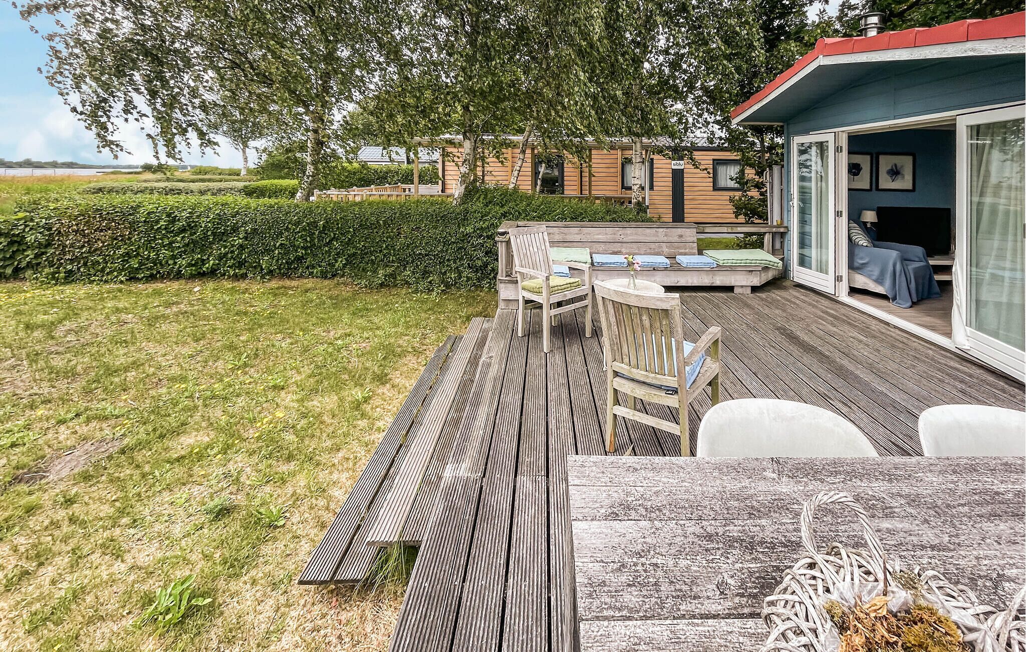 Eine Holzterrasse mit Tisch und Stühlen, ein überdachter Sitzbereich und ein Gebäude mit großen Fenstern.