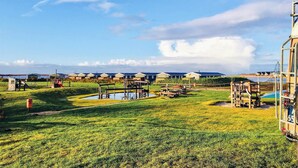 A campsite with multiple blue-roofed cabins, a playground, and a small pond.