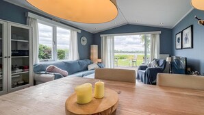A modern living room with a wooden dining table, two candles, a sofa, and a view of the outdoors.