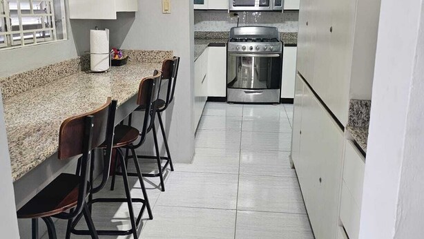 A kitchen with white cabinets, a granite countertop, a stove, an oven, and a ceiling fan. - Home away from home (Kingston)
