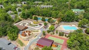 Vista aérea de una zona residencial con un camino sinuoso, una piscina, canchas de tenis y un edificio rojo.