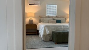 A bedroom with a bed, bedside table, lamp, air conditioning unit, and window with blinds. - In-Town Lewes, Private Getaway! 4 BDRM,2.5BA. Steps to 2nd Street and Bike Trail (Lewes)