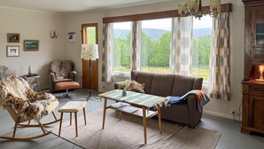 A cozy living room with a sofa, a rocking chair, a table with a quilt, and a view of a forest through large windows. - 7 bedroom amazing home in Nedre Vats (Nedre Vats)