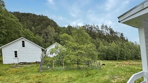 A rural setting with two white wooden houses surrounded by a grassy field and a forested hill. - 7 bedroom amazing home in Nedre Vats (Nedre Vats)
