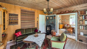 Un salon chaleureux avec une cheminée, des murs en bois, un canapé vert, une table à manger et une bibliothèque.